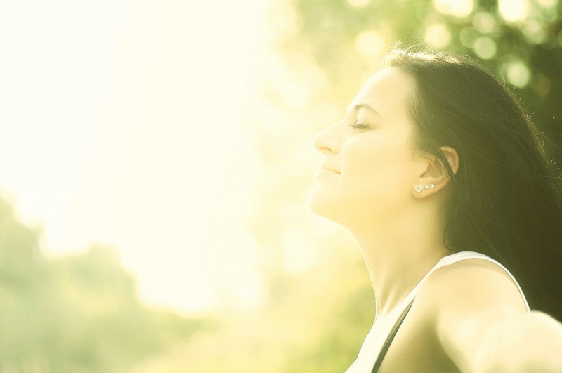 Woman enjoying the sunlight with her eyes closed in a serene, natural setting.