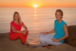 Two women sitting on rocks on the shore overlooking the sunset and the sea