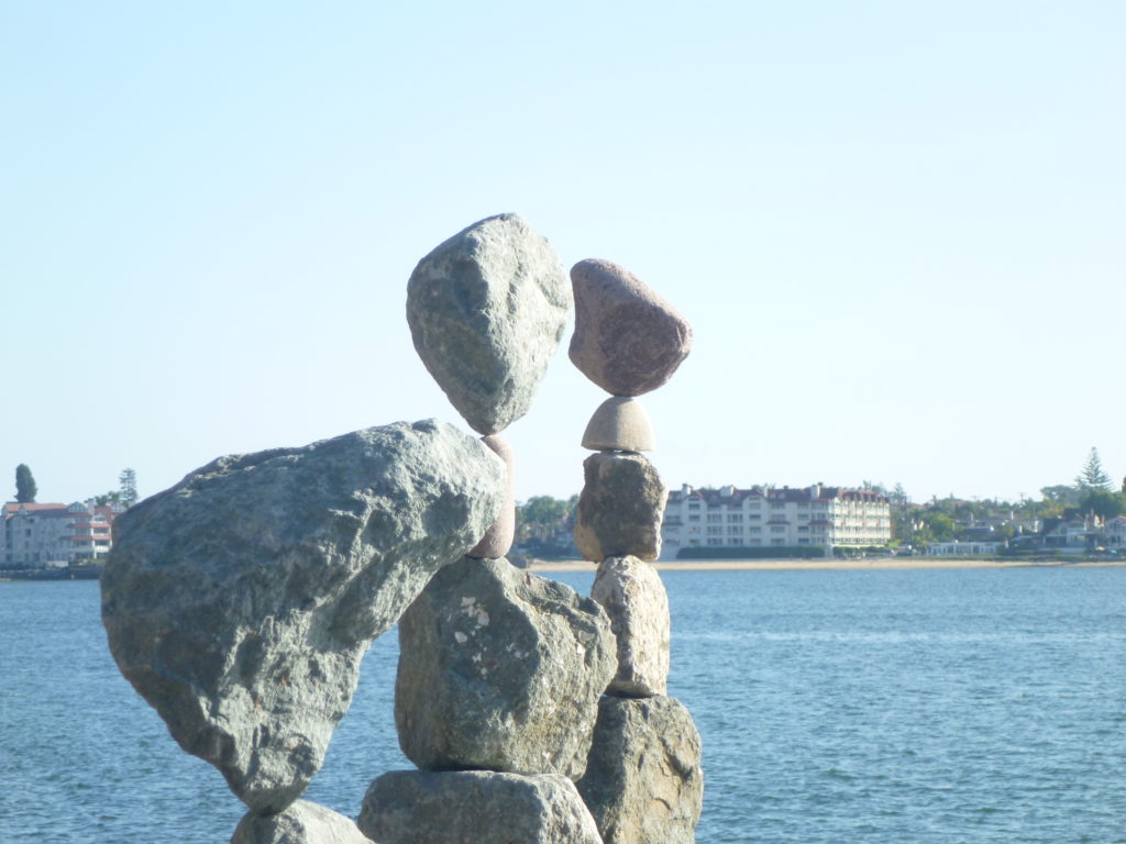 Balanced rock sculpture by a tranquil body of water.