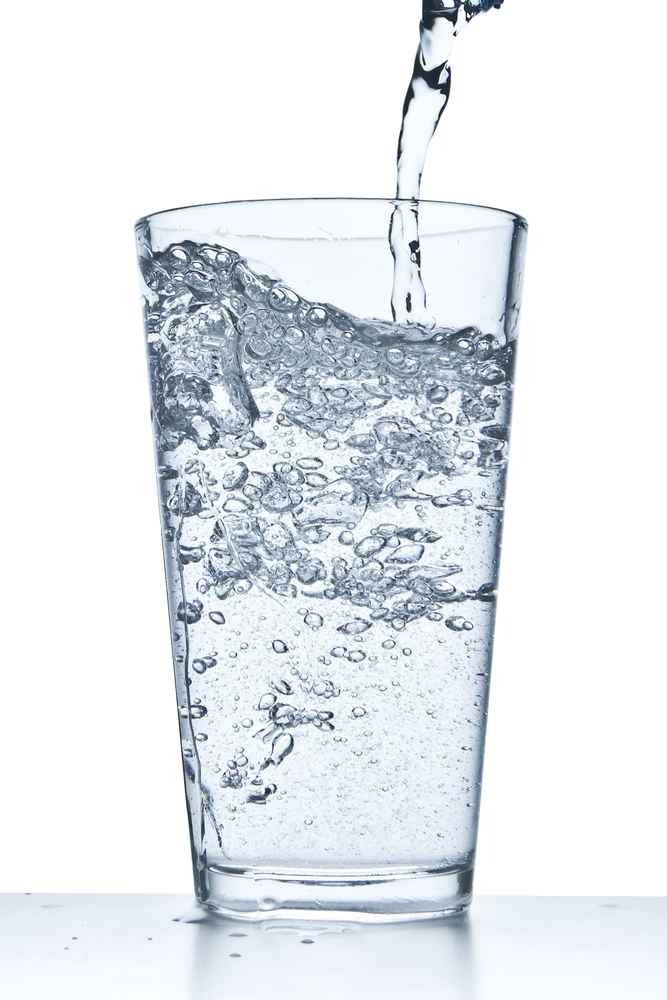 Pouring water into a clear glass, causing bubbles and a splash.