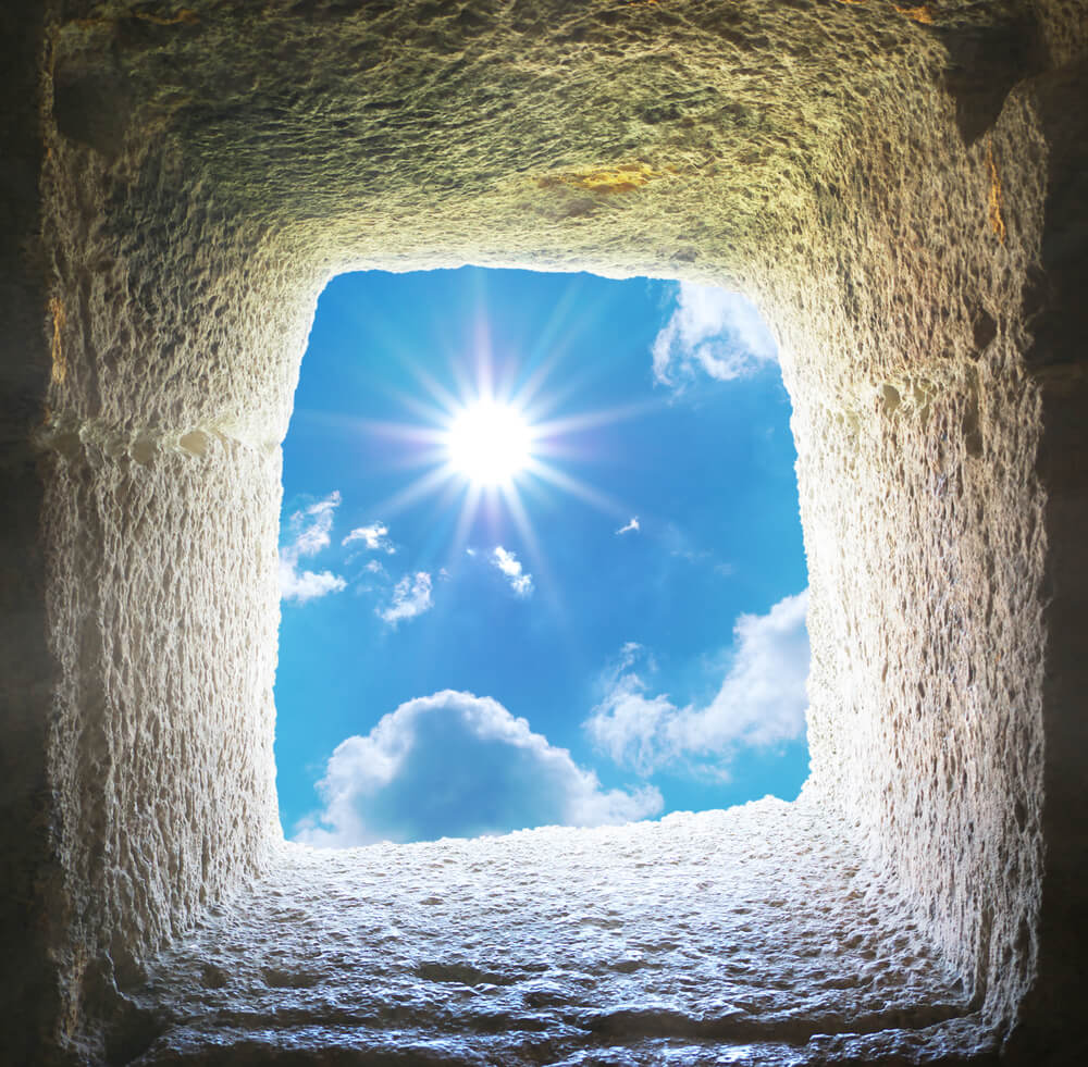 Sunlight streaming through a rugged stone window opening against a blue sky with clouds.