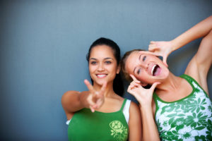 Two cheerful young women posing playfully against a blue background.
