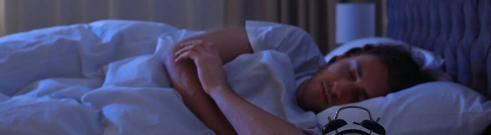 A woman sleeping in her bed at night with an alarm clock visible in the foreground.