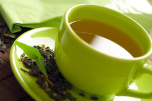A cup of green tea with loose leaves beside it.