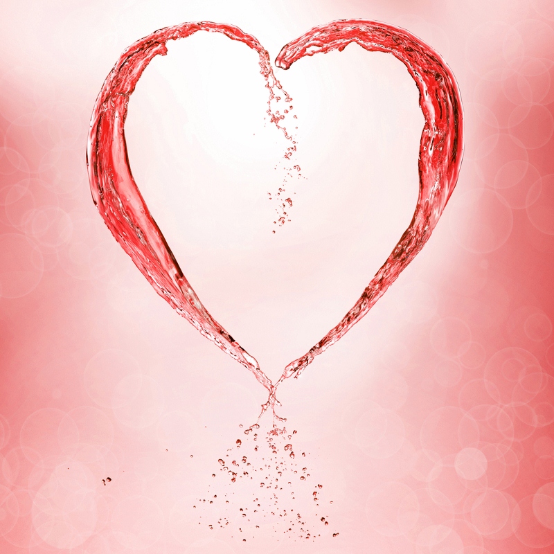 A heart shape formed by splashing red liquid on a pink background with bokeh effects.