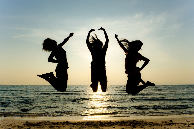 Three people jumping on a beach at sunset, silhouetted against the sky.