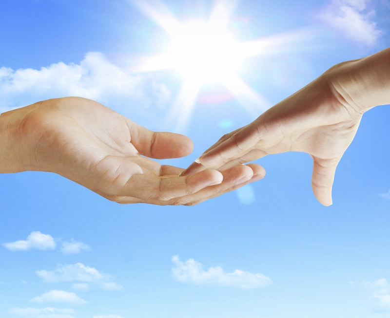 Two hands reaching towards each other against a backdrop of blue sky and sunlight.