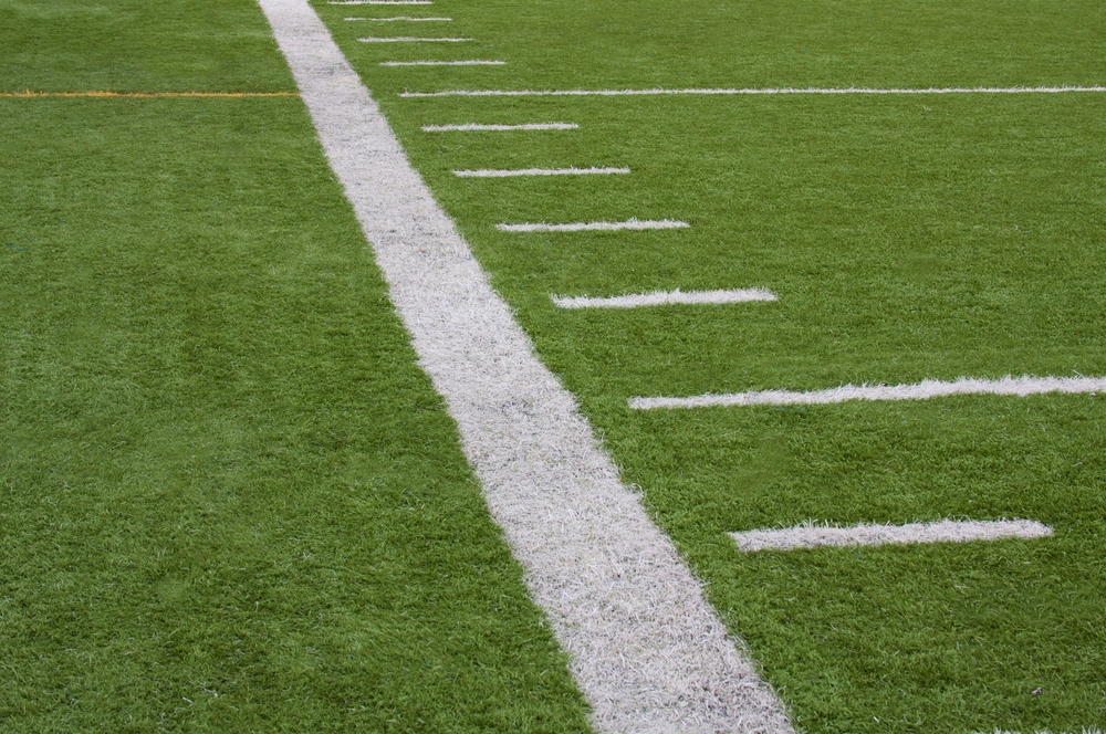 A close-up view of a synthetic grass sports field with white boundary and yard lines.