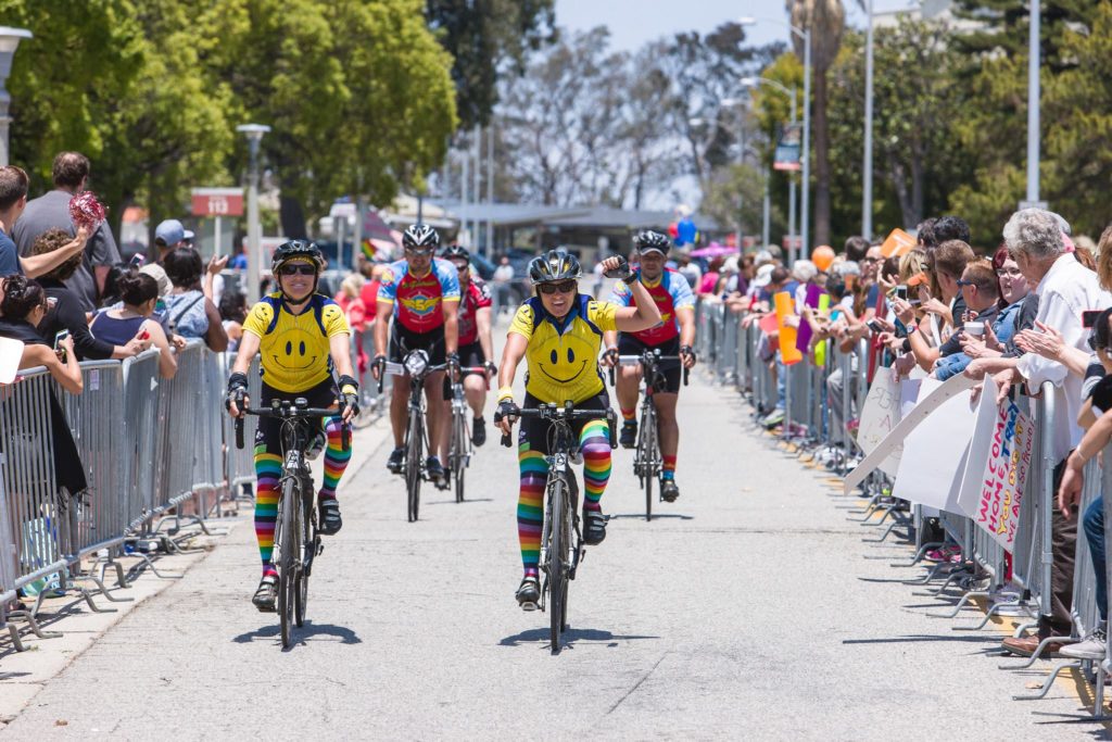 Cyclists wearing smiley face jerseys participating in a bike race with spectators lining the route.