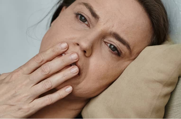 A person lies on a pillow with their hand covering part of their mouth, looking tired or unwell.