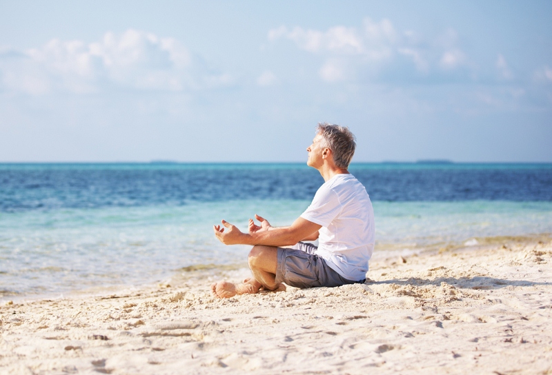 Man meditating on a sandy beach with the ocean in the background.