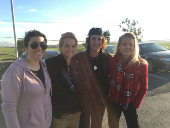 Four women smiling and posing together outdoors on a sunny day.