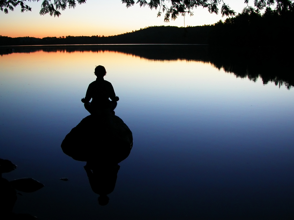 person meditating on a rock at dusk overlooking lake
