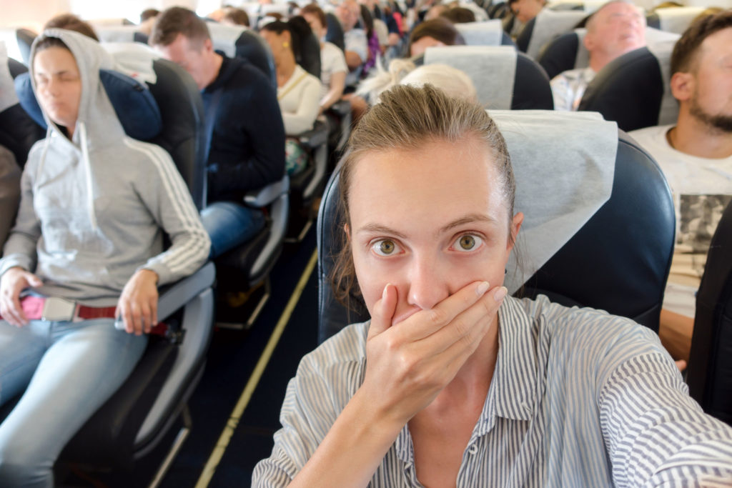 Scared woman covering mouth with hand and taking selfie in airplane.