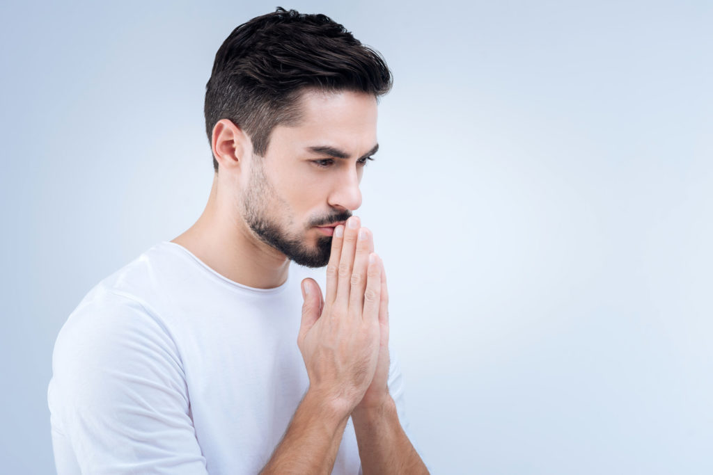 Sad young man praying while standing against the blue background