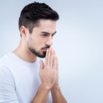 Sad young man praying while standing against the blue background